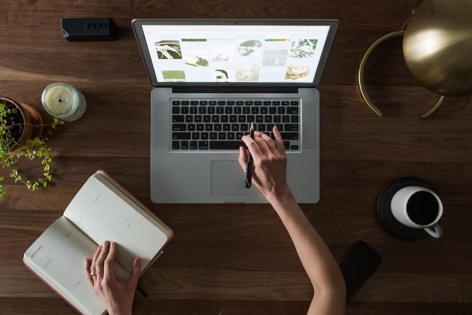 Người làm việc trên laptop bên cuốn sổ và tách cà phê — bán khoá học online ở đâu